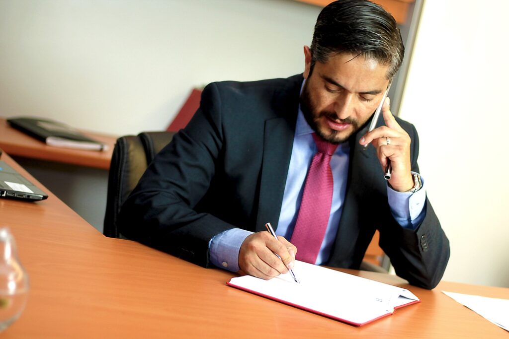 Hombre con traje hablando por teléfono mientras apunta en una libreta.